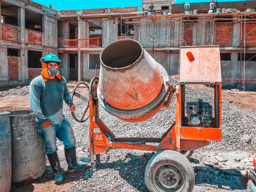 A construction worker operating a concrete mixer at an active building site, emphasizing safety gear.