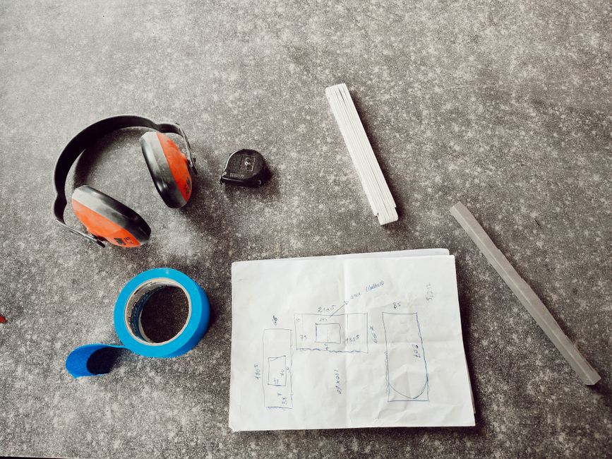 Overhead view of engineering tools including headphones, tape, and a sketch on a workbench.