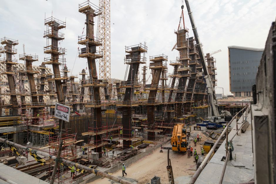 A bustling construction site with towering steel frameworks and cranes under a cloudy sky.