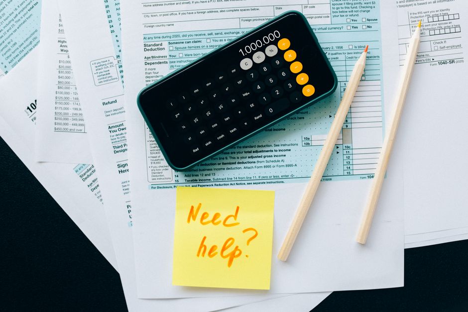 Top view of financial papers with a calculator, pencils, and a note saying ’Need help?’ indicating tax or accounting assistance.