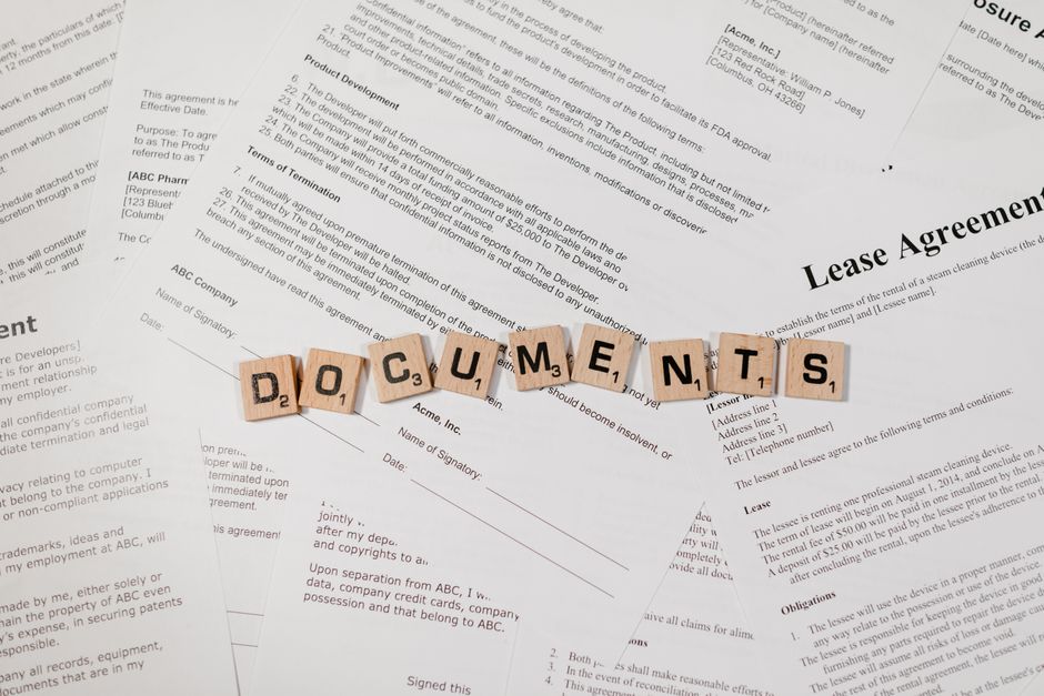 Top view of scrabble tiles spelling ’DOCUMENTS’ on various contracts and agreements.