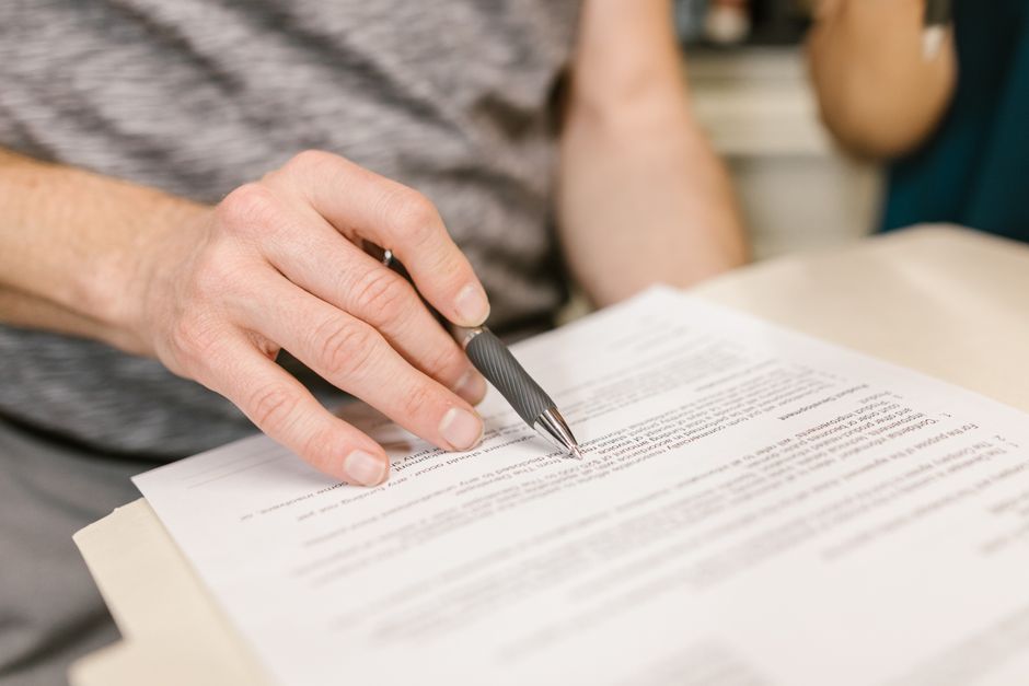 Close-up of a person’s hand signing an important legal document with a pen indoors.
